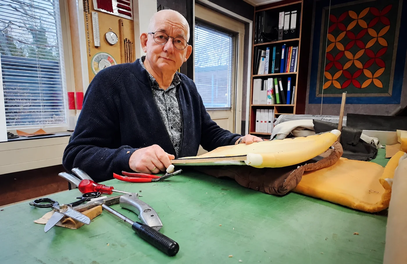 Jan Schuurkamp aan de werkbank met een stoelzitting en stoffeergereedschap